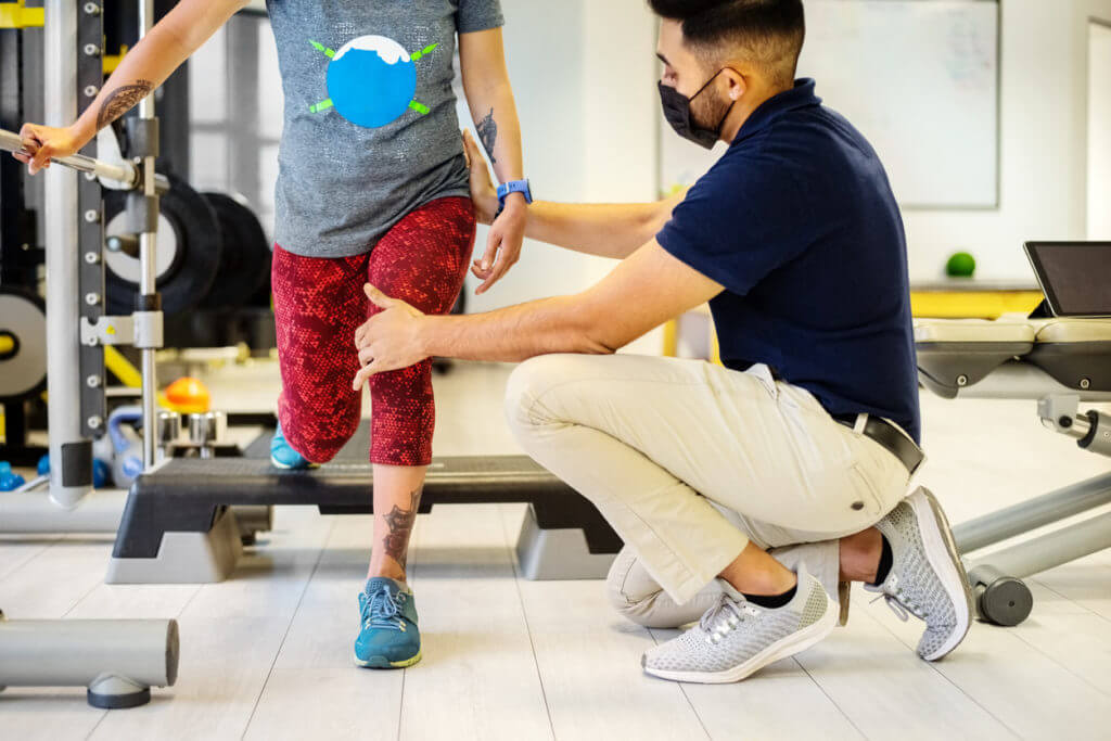 physical therapist with face mask helping woman exercise after knee replacement