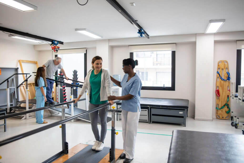 Group of people during physical therapy walking with the help of parallel bars at a physical rehab medical center 