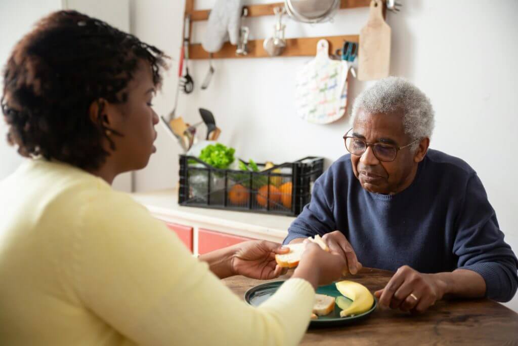 man with dementia eating with caregiver