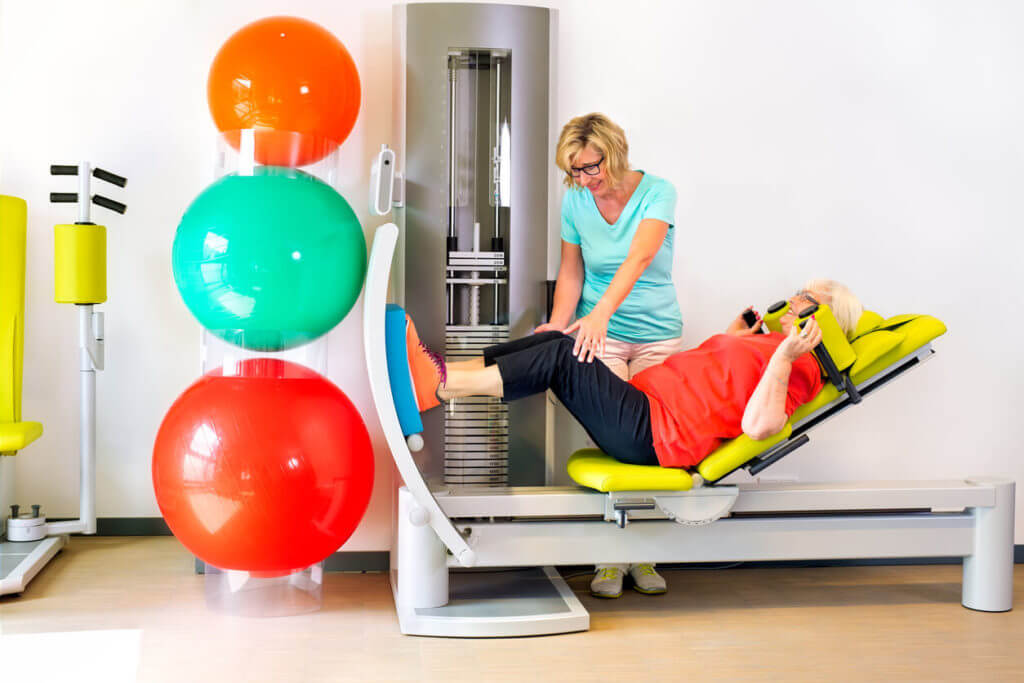 A therapist helps a woman strengthen her leg muscles during her post-operative therapy exercise routine.