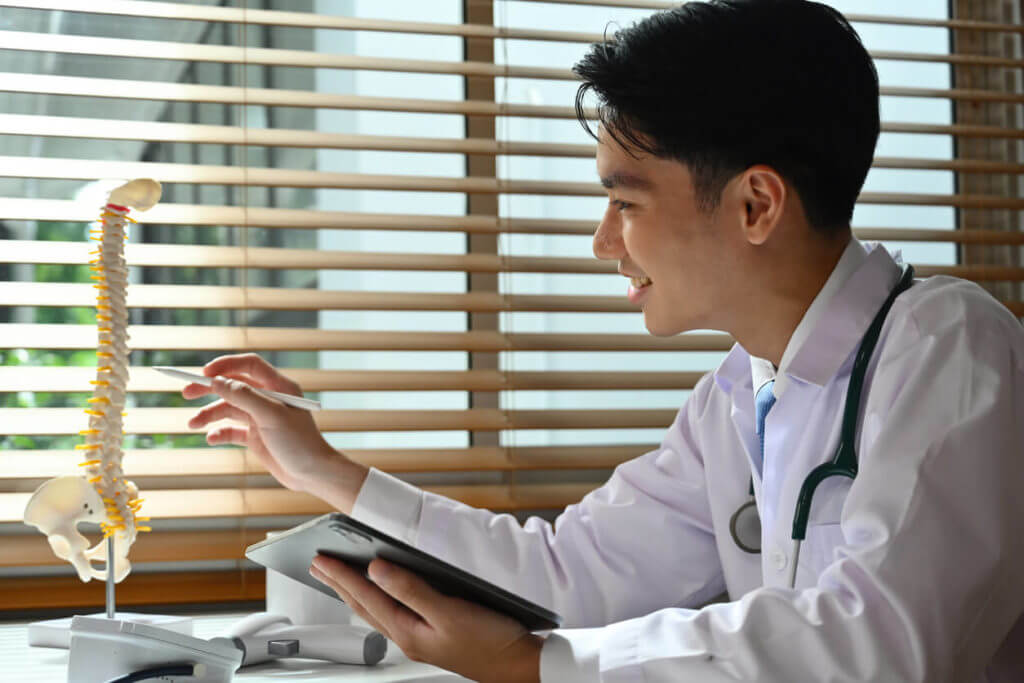 A young doctor is pointing to a spine model while explaining the treatment for a herniated disc.