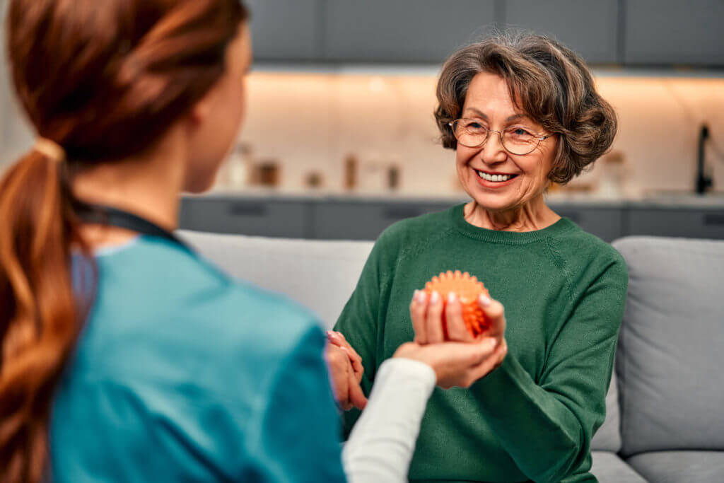 Smiling senior woman holding a spiked ball for arm rehabilitation and recovery after illness during physical therapy.